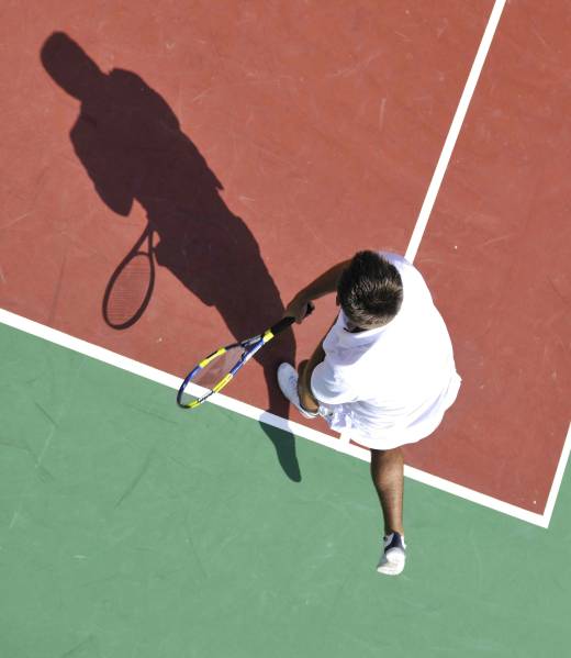 young man play tennis outdoor on orange tennis court at early morning